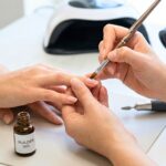 A professional nail technician applies structured builder gel to a client's natural nails using a precision brush in a clinical salon setting.