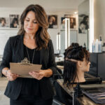 Experienced beauty instructor reviewing a clipboard beside a mannequin head and salon tools in a cosmetology classroom.