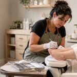 Licensed nail technician wearing clean gloves provides a careful waterless pedicure to an older woman in a private, sanitary nail studio.