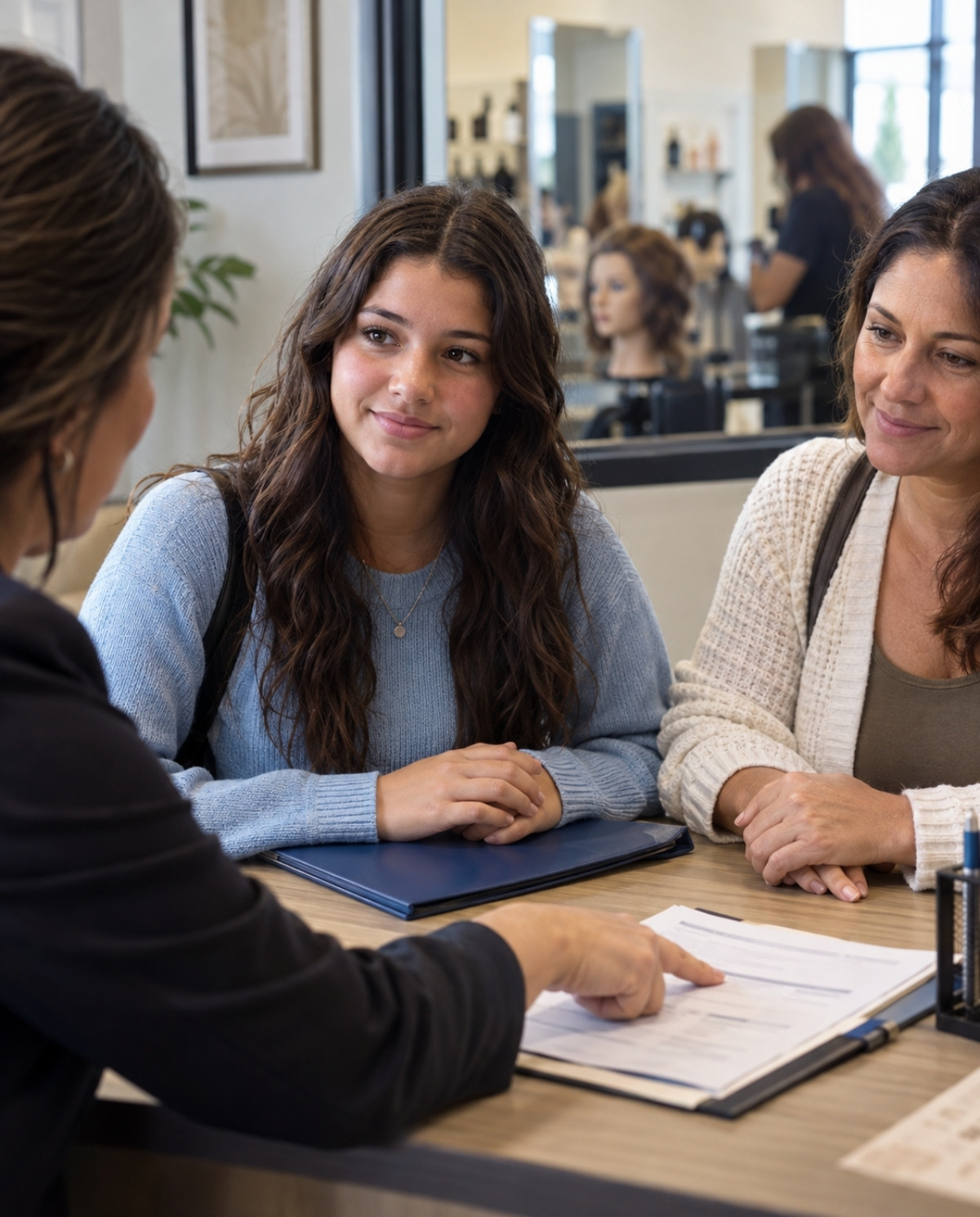 Teenage prospective cosmetology student and parent listening as an admissions adviser explains enrollment paperwork and requirements.